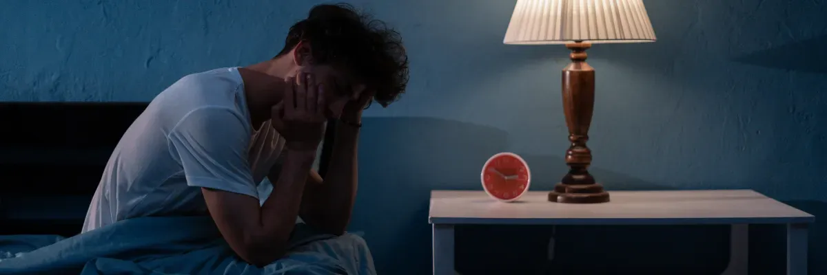 photo of a person with their head in their hands, sitting on the edge of bed, in the middle of the night